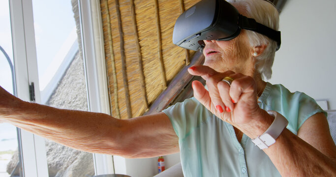 Senior woman enjoys VR technology at home, gesturing in 4K resolution.