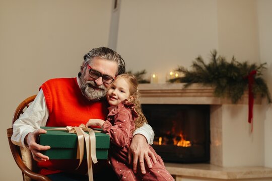 Grandfather and granddaughter sharing christmas gift by fireplace