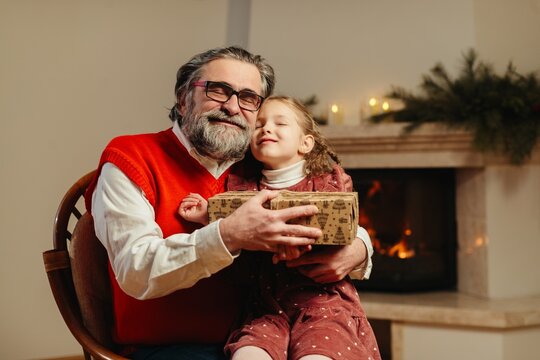 Grandfather holding granddaughter and christmas gift by fireplace
