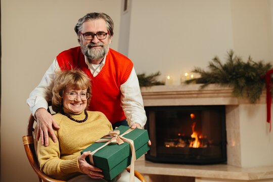 Senior couple exchanging christmas gift by fireplace