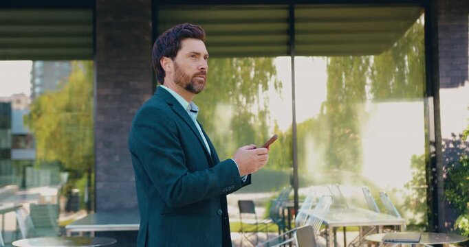 Side view of an businessman walking along a city street while using his smartphone and responding to text messages