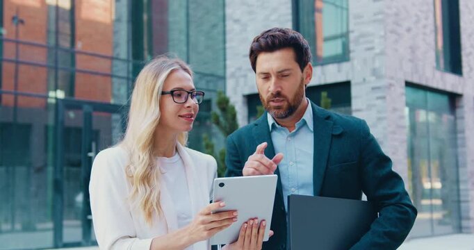 Businessman and businesswoman reviewing information on a tablet while having a professional discussion.