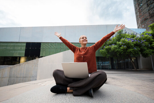 Joyful woman celebrates success with laptop outdoors