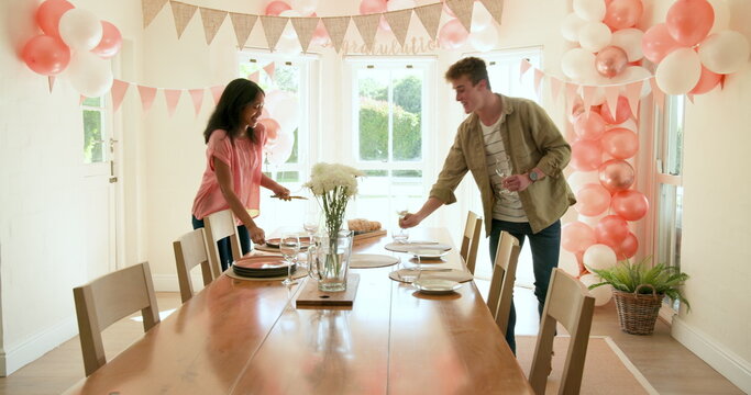 Happy white, black and multiracial friends preparing plates and decorations for party at home with c