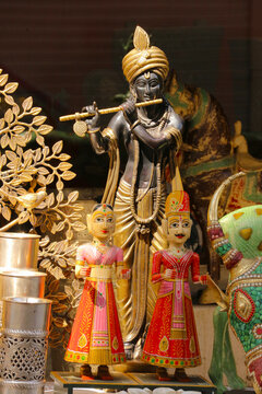 A brass statue of Lord Krishna with traditional Rajasthani Kathputli wooden puppets at a shop.