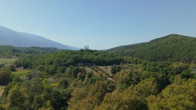 Aerial drone flight smoothly sweeping over dense green forest canopy to reveal the historic Tsar Samuil sculpture monument standing amidst lush natural surroundings in Bulgaria.