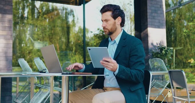 Businessman in formal attire working outdoors with laptop and tablet