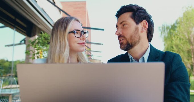 Businessman and businesswoman discussing work while looking at laptop screen outdoors