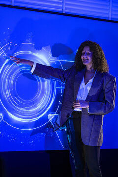Businessman and businesswoman raise a stylus to highlight a detail beside a glowing padlock hologram and digital world map inside a futuristic office illuminated by glowing blue projections