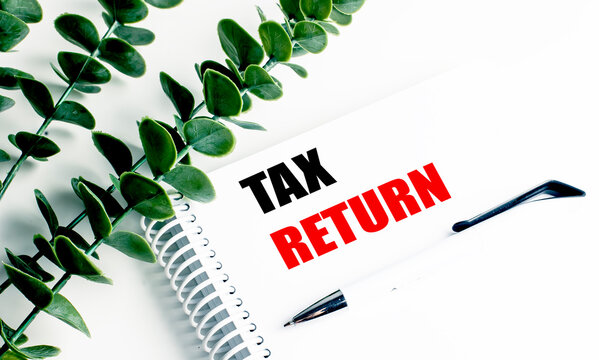 Tax return concept with notebook, pen and green leaves, representing personal finance, income reporting and annual filing