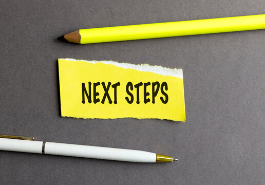 Next steps text on yellow paper with pencil and pen on a gray background, action planning and strategy concept