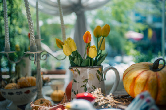 yellow tulips inside vintage pitcher near striped pumpkin, cozy autumn harvest decoration featuring floral arrangement and tall candles indoors