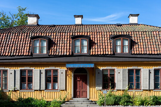 Traditional yellow wooden house in Stockholm with red tile roof and shuttered windows
