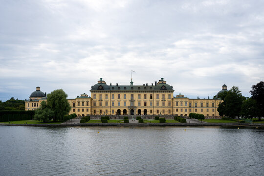 Drottningholm Palace stands beside the water beneath a broad, overcast sky in Stockholm