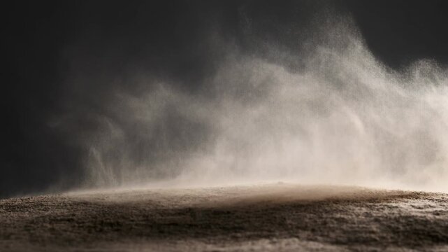 Windblown dust sweeps across barren desert ground beneath a dark atmospheric sky. Weather documentaries, environmental campaigns, and climate change education.