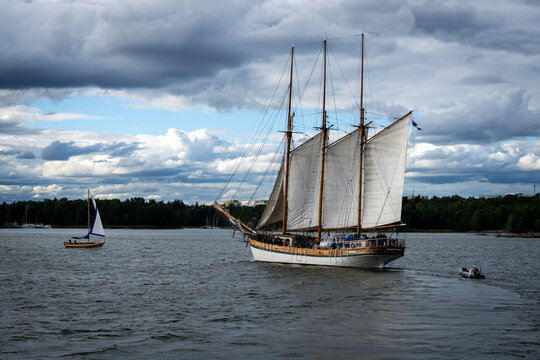 A traditional three-masted sailing ship crosses the water beneath dramatic Helsinki skies
