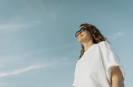 Beautiful millennial girl smiling and looking away on a bright sunny day, view from below.
