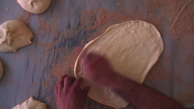 Overhead view of hands pressing parallel ridges into dough on a wooden table
