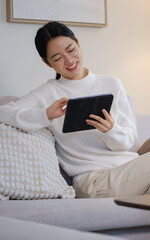 Woman smiling while using a tablet on her sofa. © wattana