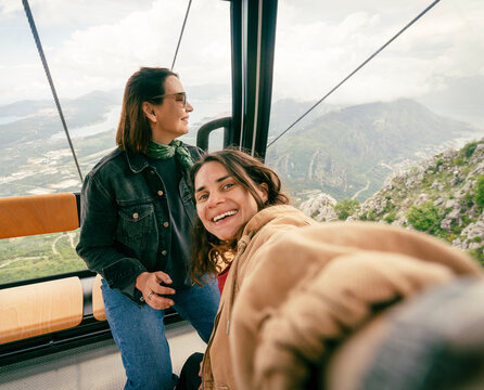 Two happy female friends taking selfie with smartphone inside Kotor cable car cabin