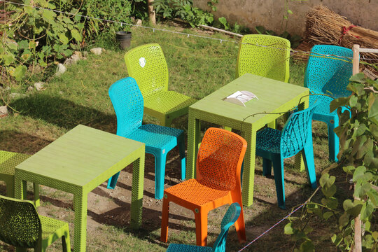 Bright colorful plastic tables and chairs on a green lawn at an outdoor cafe.