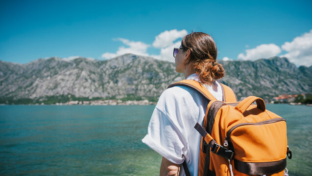 Back view of young woman traveler with orange backpack admiring scenic view of Kotor Bay&nbsp;