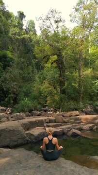 Woman sitting in yoga pose by tranquil stream in forest young practicing