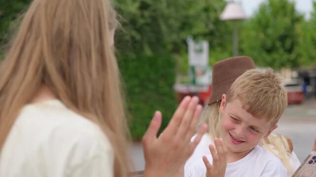 A teenage girl is teaching a boy a hand clapping game while sitting on a bench in the park with mother