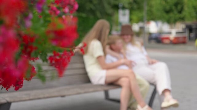 Woman and two children laughing together on a wooden bench with flowers in the foreground