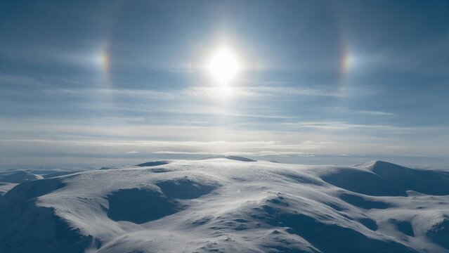 Spectacular symmetrical sun dog rainbow phenomenon with bright parhelia framing the winter sun over snowy mountain peaks.