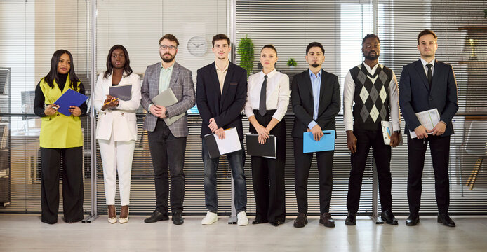 Candidates businesspeople group portrait in office meeting lineup. Diverse professionals hold resumes and folders for recruitment. Great for HR and hiring. Clear staffing and selection concept.