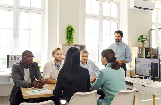 Business team colleagues discuss strategy during meeting. Diverse professionals share ideas around documents and analytics in a bright workspace. Teamwork enables clear business decisions.
