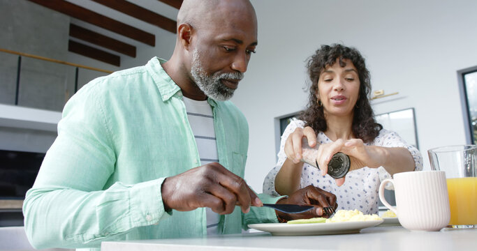 Happy couple having breakfast and seasoning scrambled eggs in kitchen