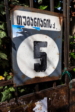 Rusty house number sign showing five on an iron fence with ivy, Tbilisi, Georgia