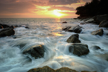 Golden sunset over sea with waves hitting rocks in Phuket © Phanicha