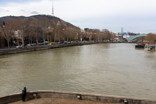 Angler fishing on the bank of the Kura river with a television tower on the hill, Tbilisi, Georgia
