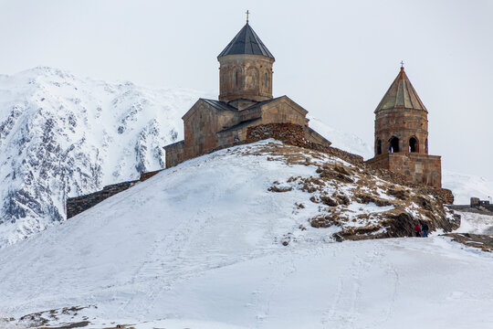 Visitors climbing a snowy hill toward Gergeti Trinity Church also called Tsminda Sameba, Mtskheta-Mtianeti, Stepantsminda, Georgia