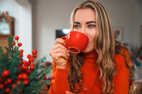 Woman drinking from a red cup beside holiday decorations indoors