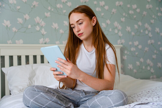 Girl sitting on a bed and using a tablet at home