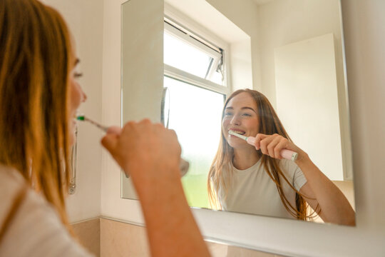 Woman brushes her teeth while looking in a bathroom mirror