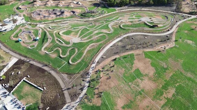 Paved distribution yard borders manicured property line Panther Creek Parkway alongside grassy sports berms along DFW Metroplex. Green turf patches border sculpted jump lines, Frisco, Texas