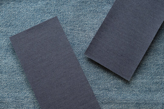Two dark denim fabric swatches arranged on blue jeans textile. Textile material and garment design concept. Fashion industry, clothing production and fabric selection. Top view, copy space.