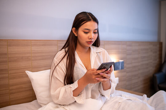 Young woman on bed in cozy bedroom using smartphone and browsing online modern lifestyle digital communication and everyday leisure.	