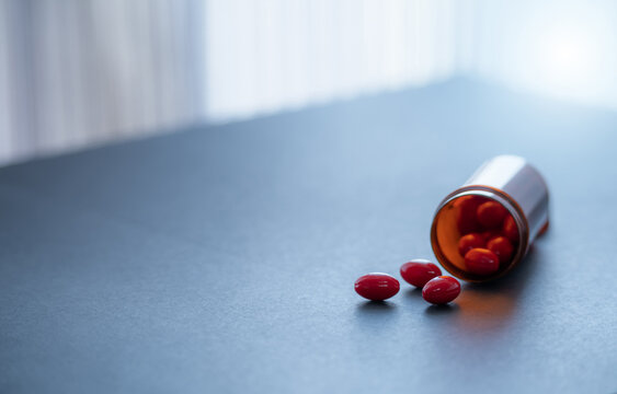 Red capsule pills and brown plastic drug bottle. Codeine and guaifenesin capsule pills to relieve coughing. Cough medicine. Opioids or narcotics drugs. Prescription drug. Cough suppressant medicine.