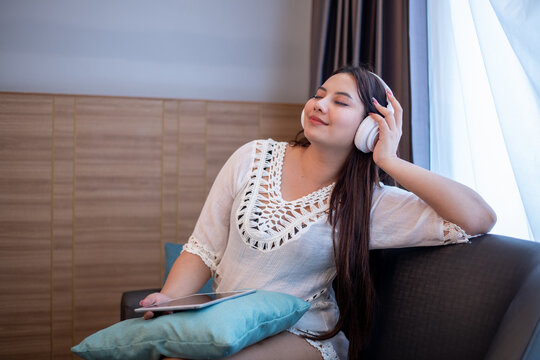 Young woman relaxing on bed while using a laptop and wearing headphones enjoying music or online content.	