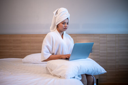 Young woman relaxing on bed while using a laptop and enjoying music or online content.	