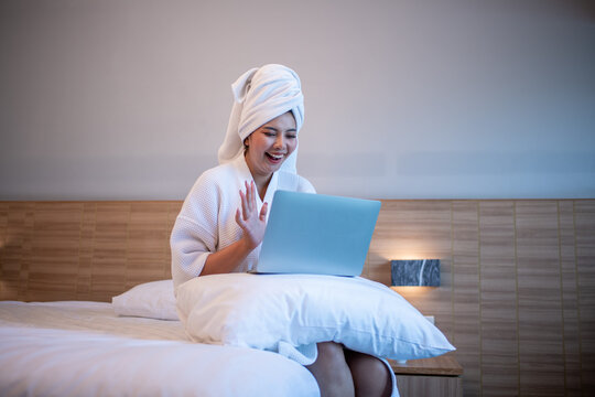 Young woman relaxing on bed while using a laptop and enjoying music or online content.	