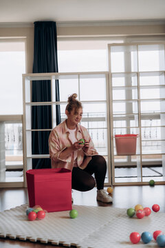 Person kneeling near cube container and bright sensory balls against large apartment windows conveys independent household work and practical toy storage in modern living space for flexible living.