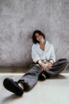 Agile workspace seamless connectivity choice lets happy Caucasian female freelancer smile warmly while sitting on floor against rustic concrete wall backdrop, maintaining personal autonomy