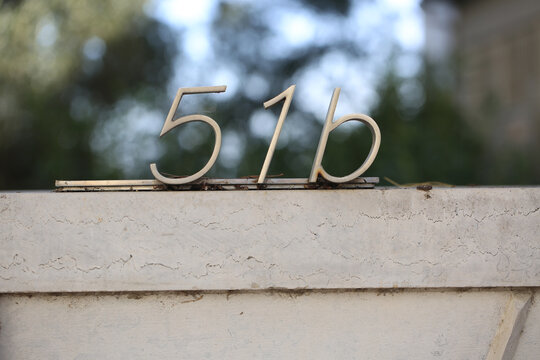 Number 51b stainless steel house number letters on limestone wall top against blurred trees with sky, brushed metal address sign detail for real estate, architecture and street numbering concepts